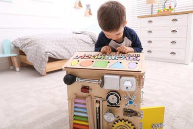 Photo of Little boy playing with busy board house on floor at home