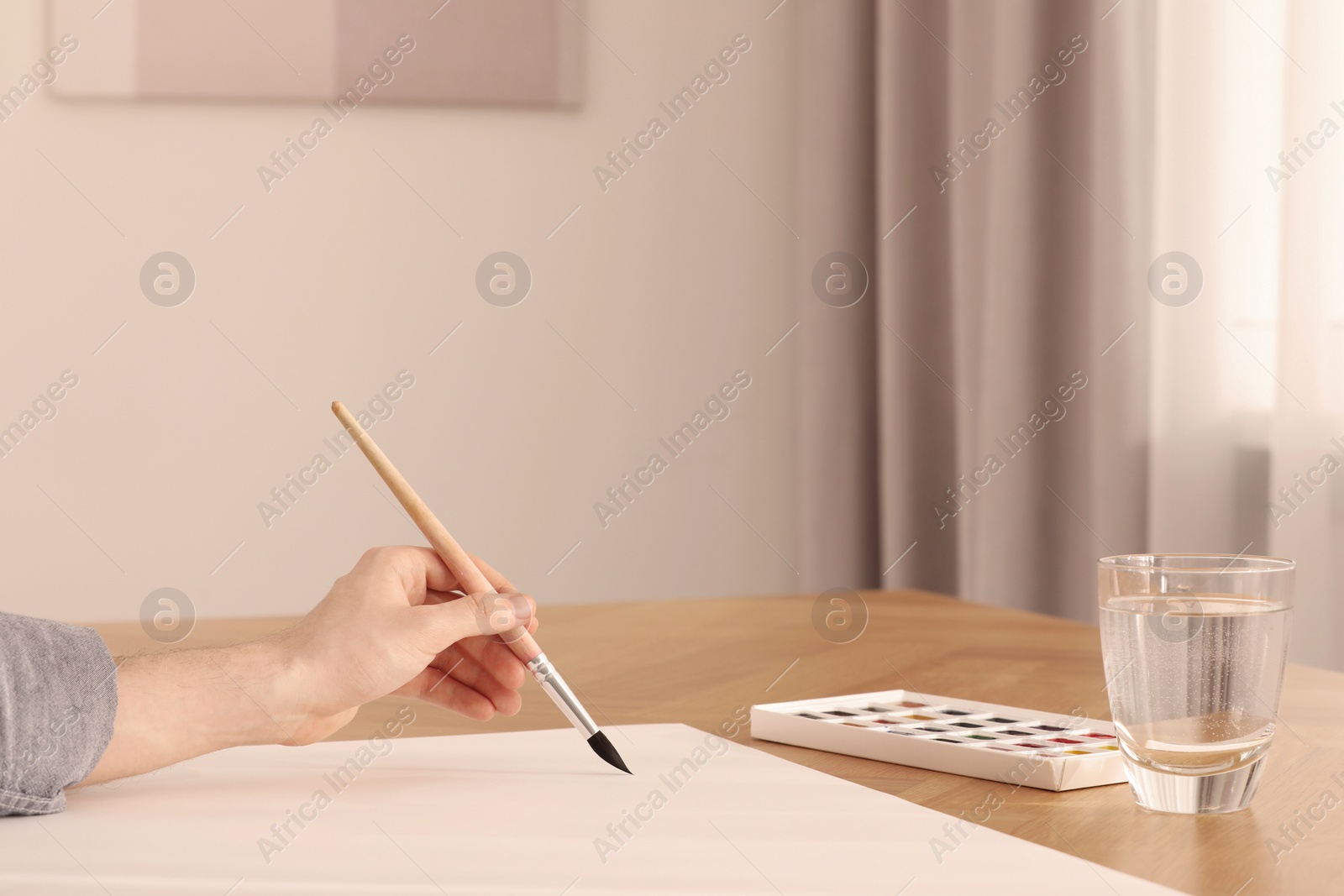 Photo of Woman with brush and paint at wooden table indoors, closeup. Watercolor artwork
