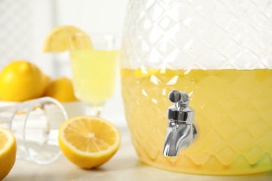 Photo of Beverage dispenser with delicious lemonade on light table, closeup. Space for text