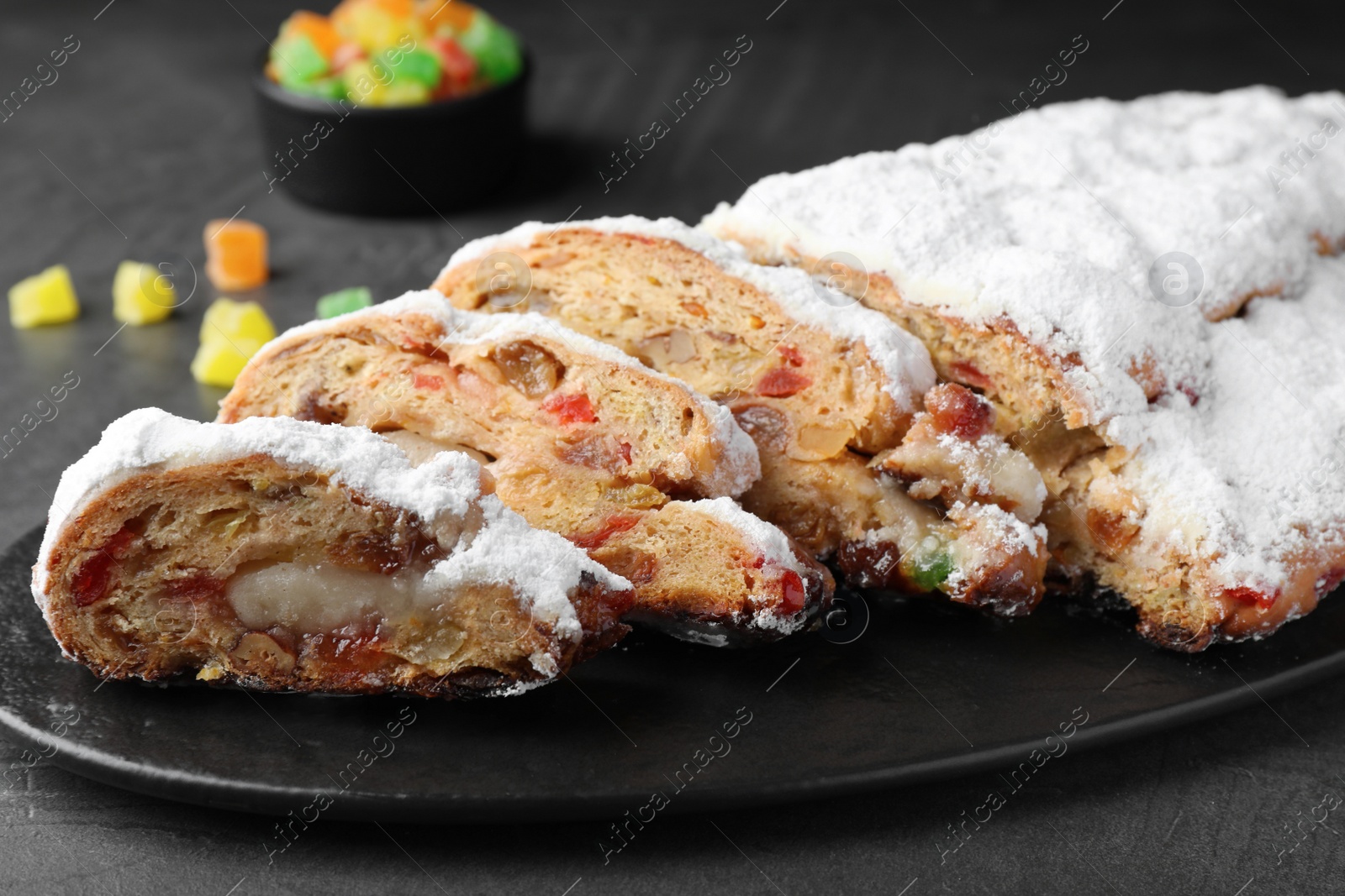 Photo of Traditional Christmas Stollen with icing sugar on black table, closeup
