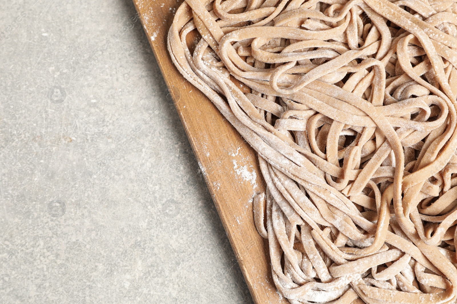 Photo of Uncooked homemade soba with wooden board on light table, top view. Space for text