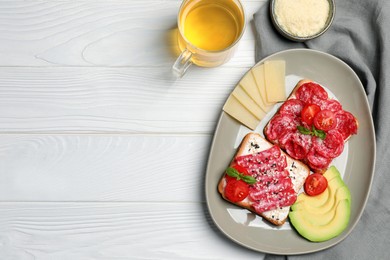 Tasty toasts with slices of sausages, tomatoes and cheese on white wooden table, flat lay. Space for text