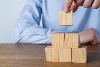 Photo of Man building pyramid of cubes on wooden table, closeup. Space for text