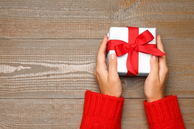 Young woman holding Christmas gift on wooden background, top view. Space for text