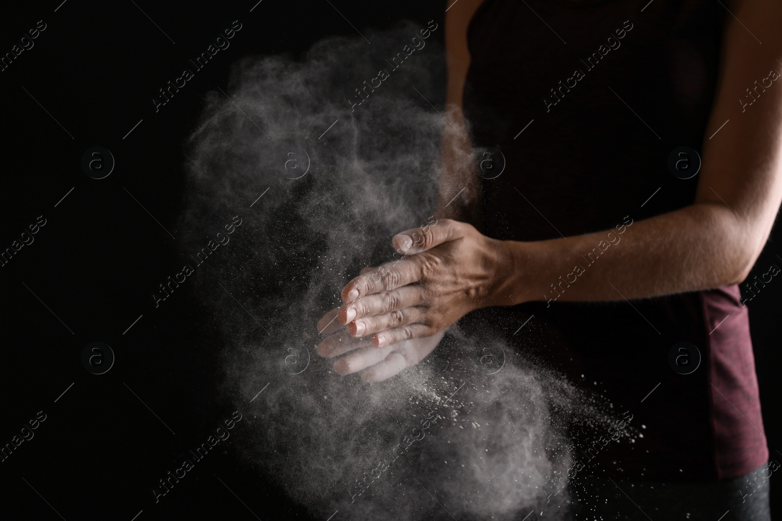 Photo of Young woman applying chalk powder on hands against dark background