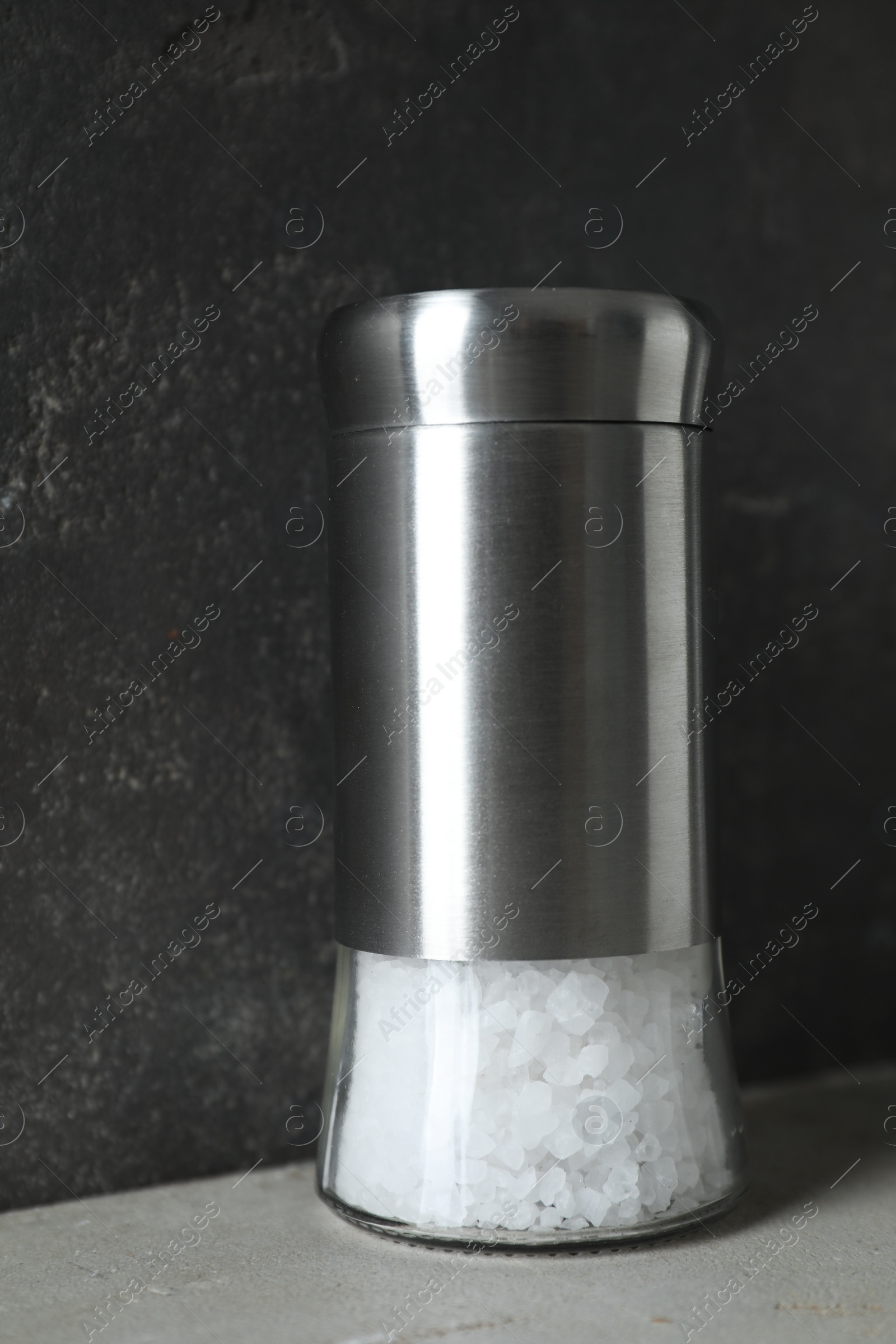 Photo of Salt shaker on light table against grey background, closeup