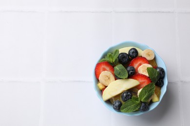 Tasty fruit salad in bowl on white tiled table, top view. Space for text