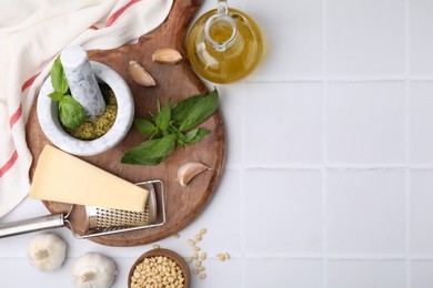 Different ingredients for cooking tasty pesto sauce on white tiled table, flat lay. Space for text