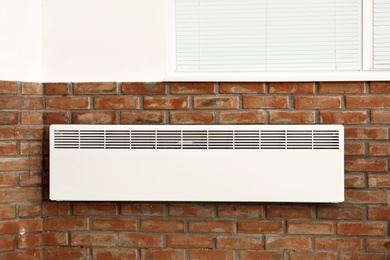 Modern heating convector on brick wall indoors