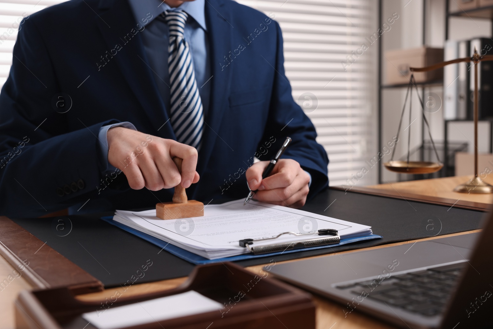 Photo of Notary with pen stamping document at table in office, closeup