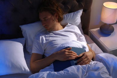 Photo of Handsome young man sleeping with book on pillow at night. Bedtime