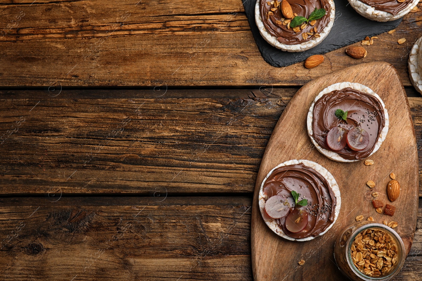 Photo of Puffed rice cakes with chocolate spread and grape on wooden table, flat lay. Space for text