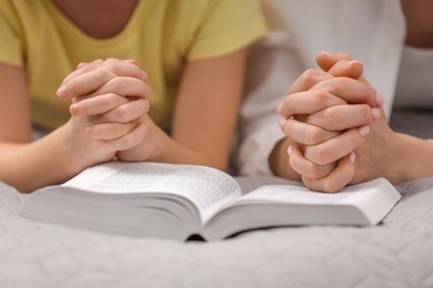 Photo of Girl and her godparent praying over Bible together indoors, closeup