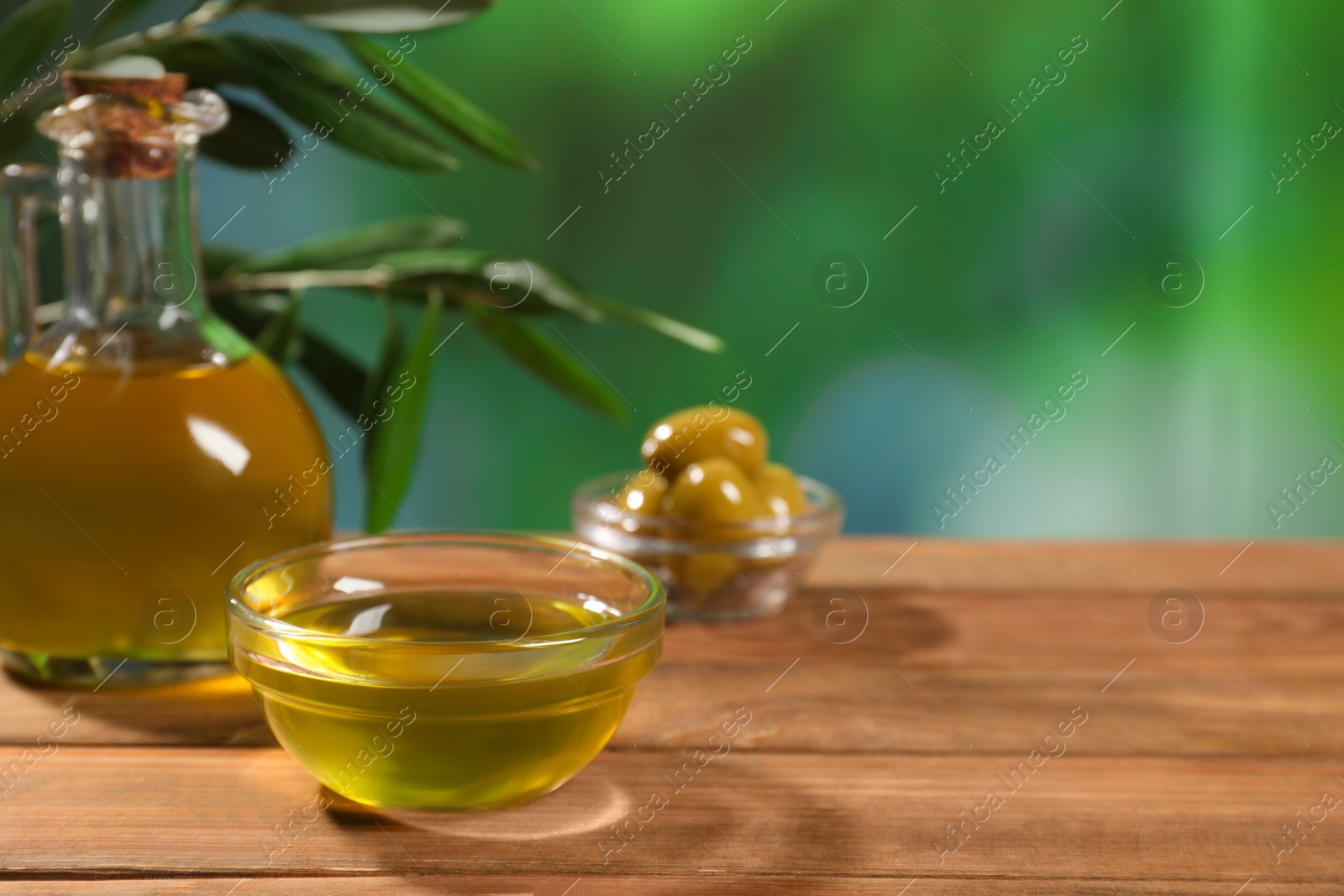 Photo of Cooking oil, olives and green leaves on wooden table against blurred background. Space for text