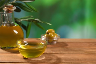 Photo of Cooking oil, olives and green leaves on wooden table against blurred background. Space for text