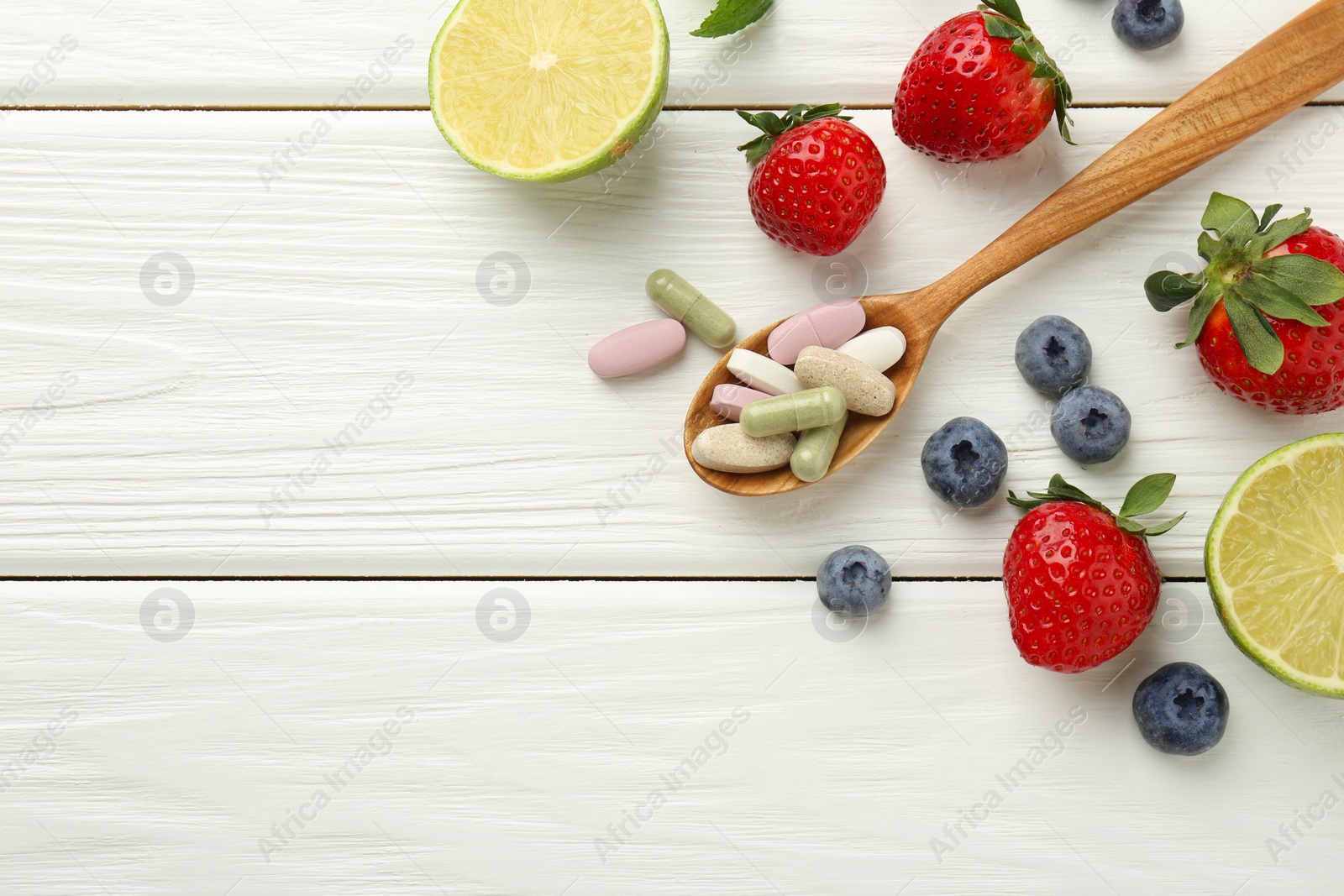 Photo of Different vitamin pills in spoon and fresh fruits on white wooden table, flat lay. Space for text