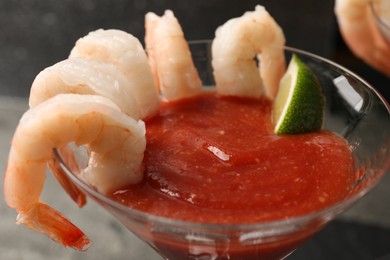Photo of Tasty shrimp cocktail with sauce and lime in glass on blurred background, closeup