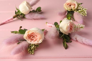 Photo of Many small stylish boutonnieres on pink wooden table, closeup