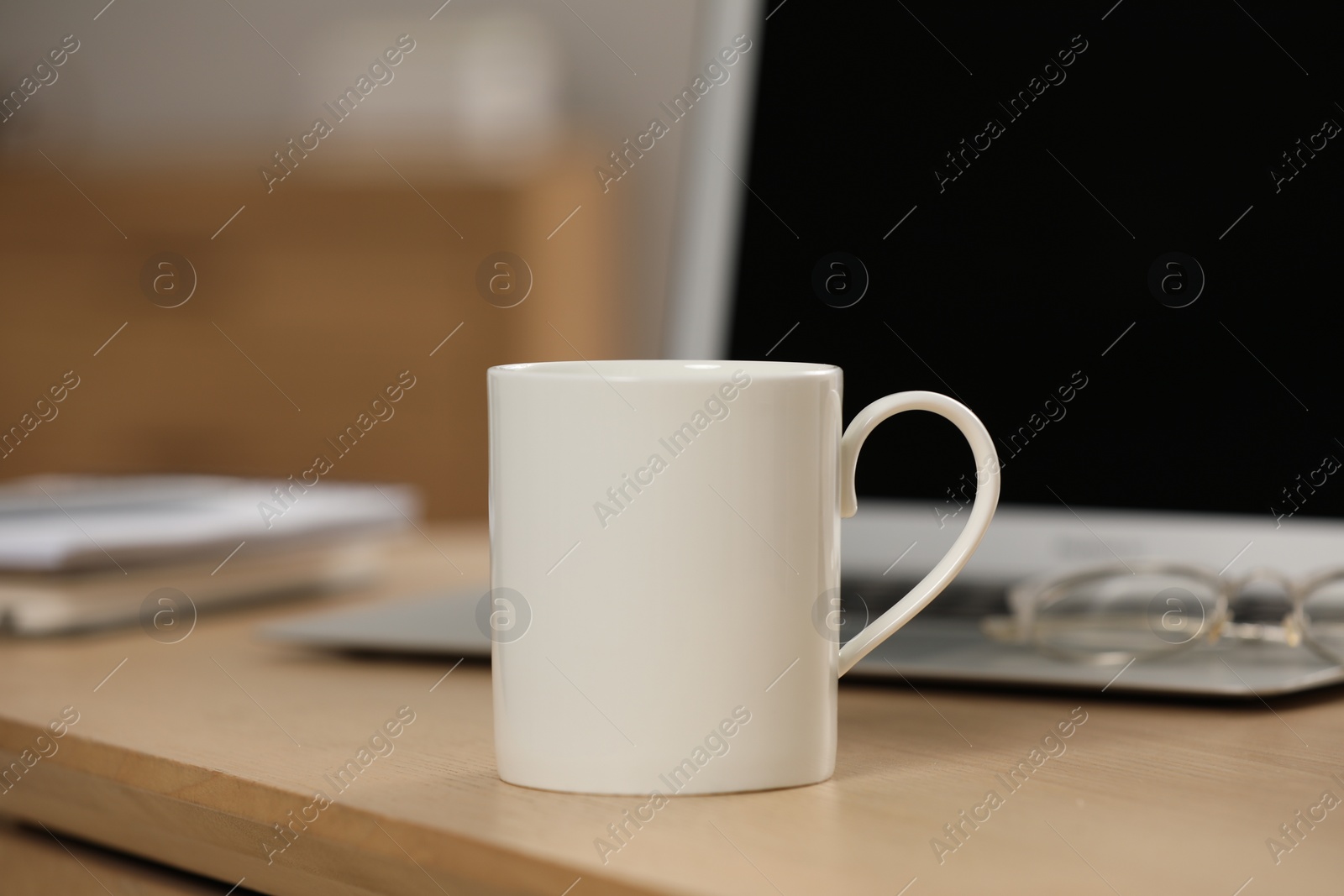 Photo of White ceramic mug and laptop on wooden table at workplace