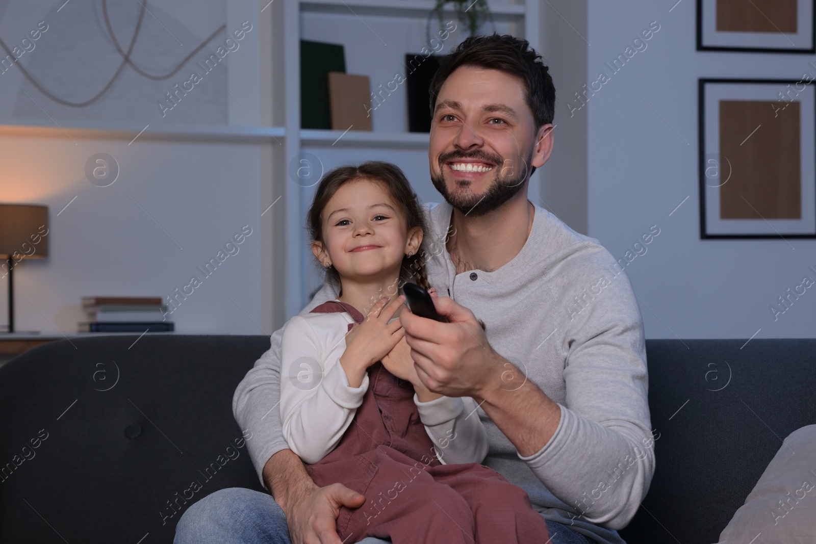 Photo of Father and daughter at home. Happy man changing TV channels with remote control