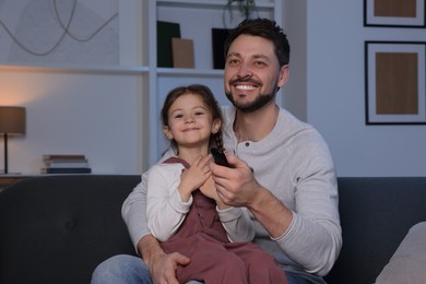 Photo of Father and daughter at home. Happy man changing TV channels with remote control