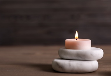 Spa stones and burning candle on wooden table. Space for text