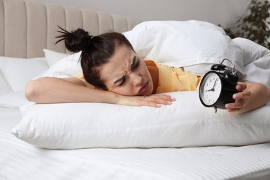 Photo of Emotional overslept woman with alarm clock in bed. Being late concept