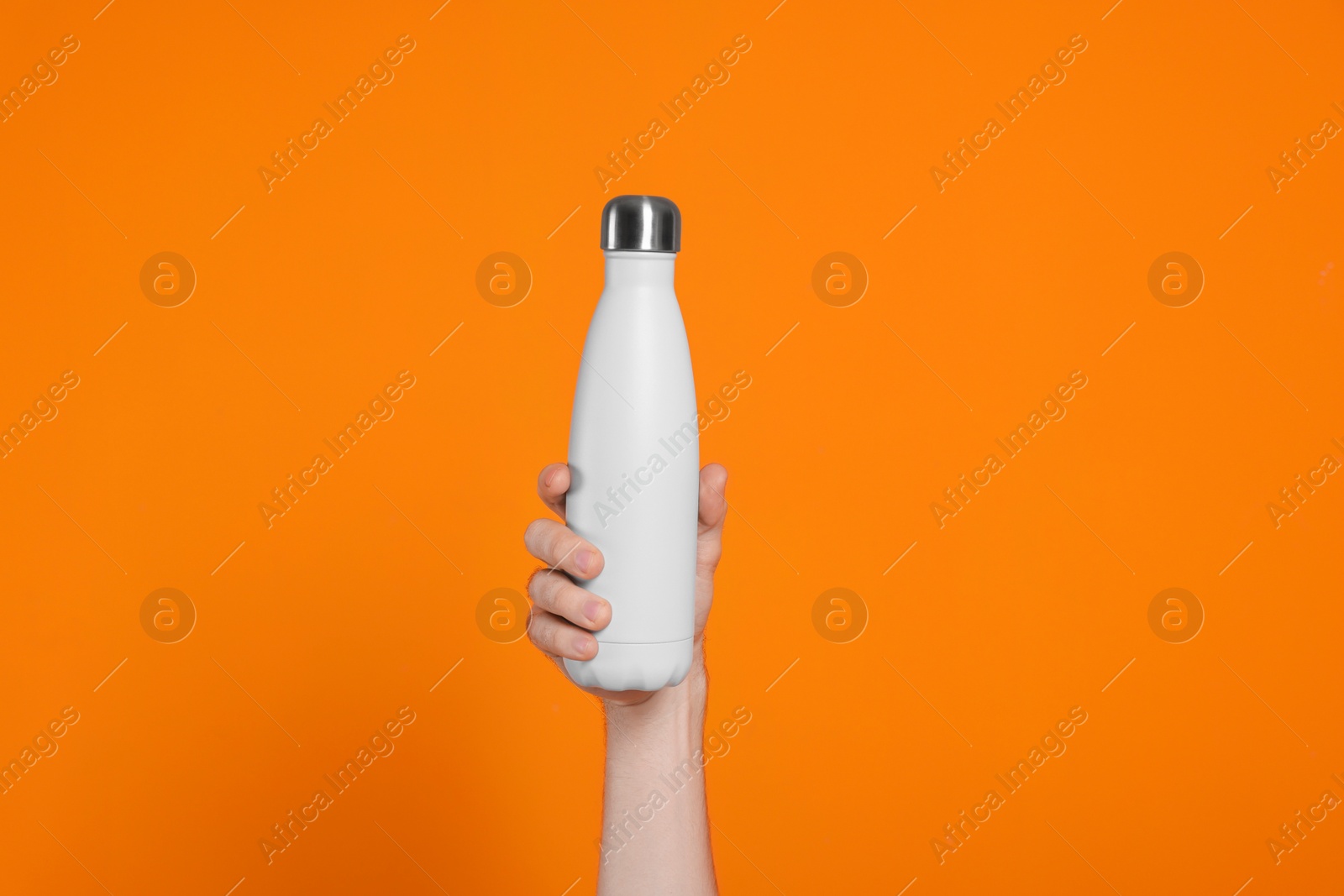 Photo of Man holding thermo bottle with drink on orange background, closeup