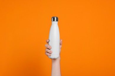 Man holding thermo bottle with drink on orange background, closeup