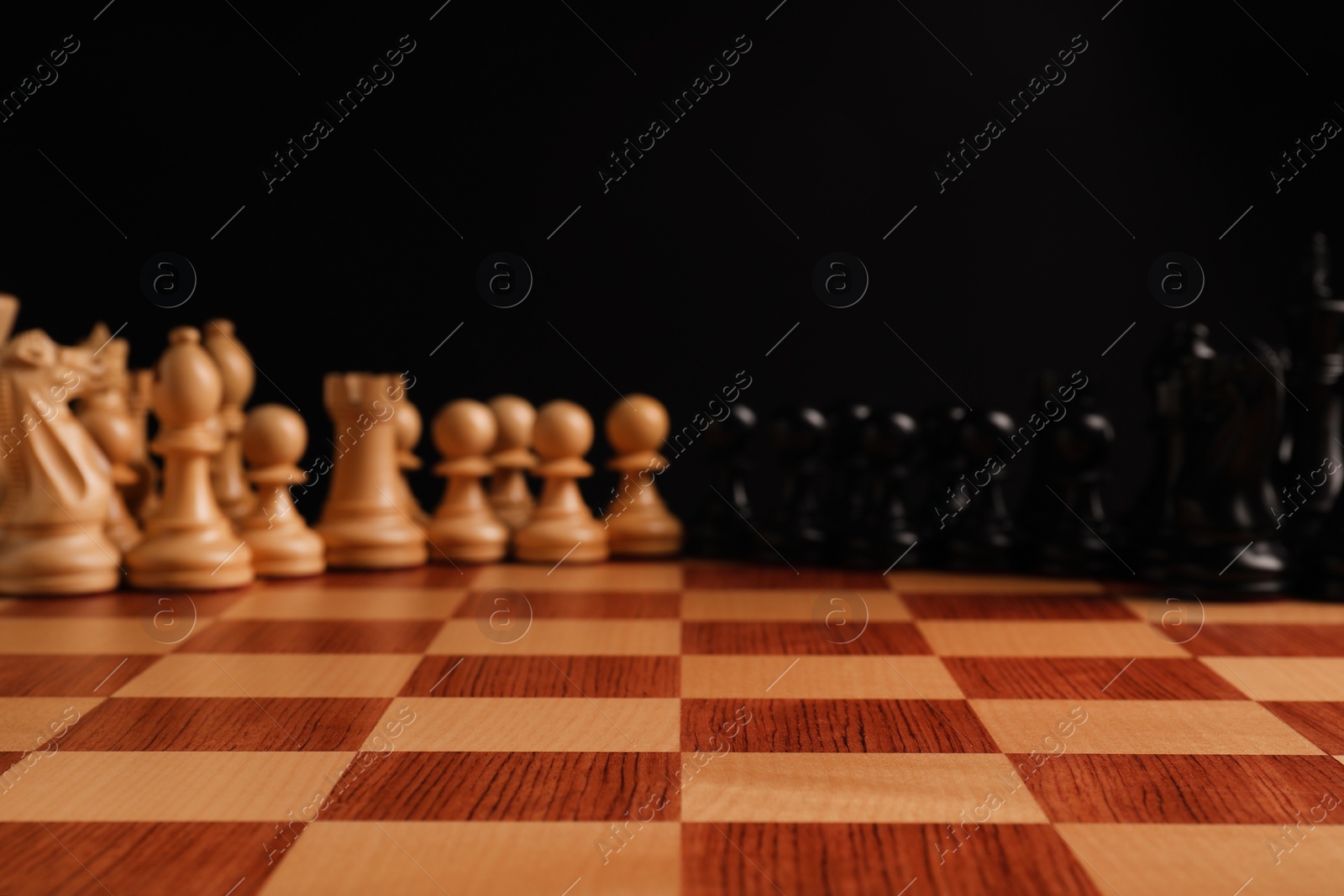 Photo of Many chess pieces on wooden checkerboard against black background, selective focus