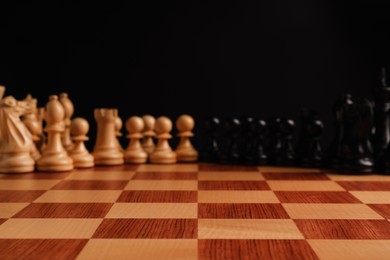 Photo of Many chess pieces on wooden checkerboard against black background, selective focus