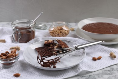Whisk with chocolate cream and ingredients on white marble table