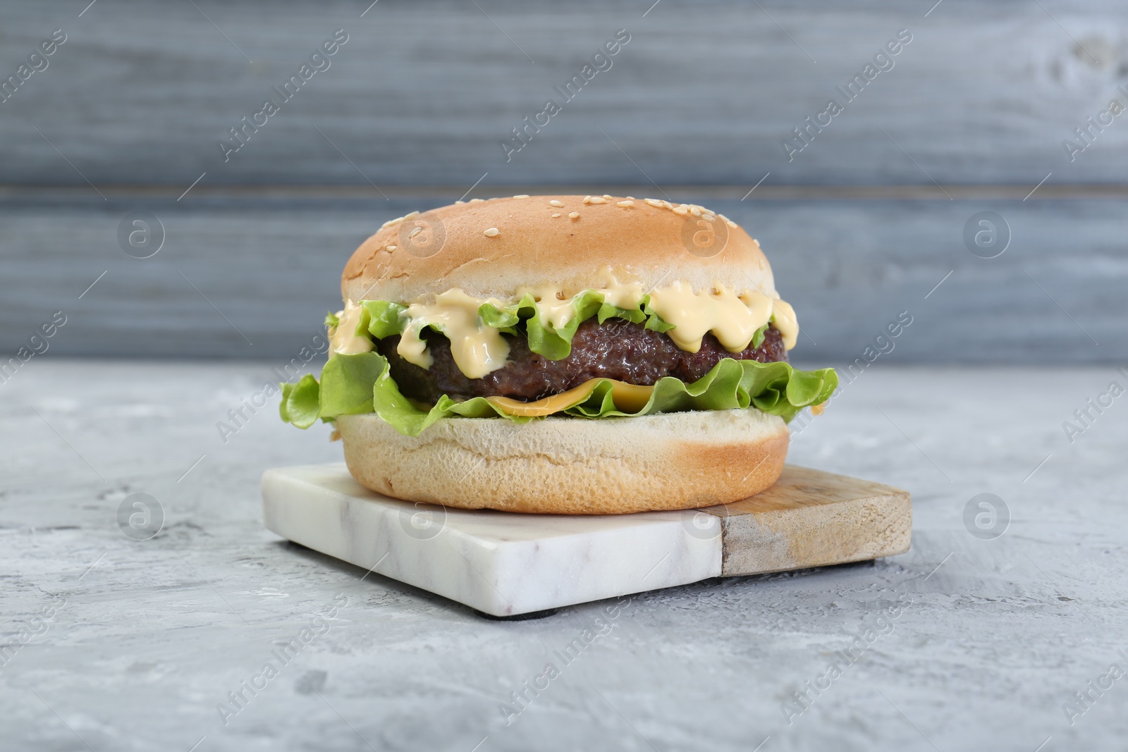 Photo of Delicious cheeseburger with lettuce, sauce and patty on grey textured table