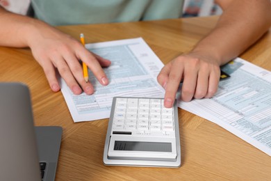 Photo of Man calculating taxes at wooden table in room, closeup