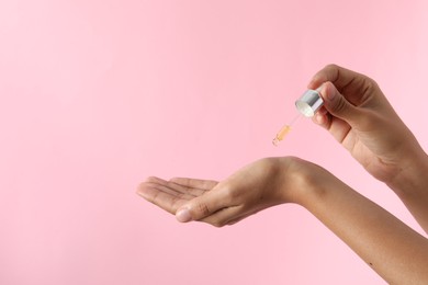 Photo of Woman applying cosmetic serum onto her hand on pink background, closeup. Space for text