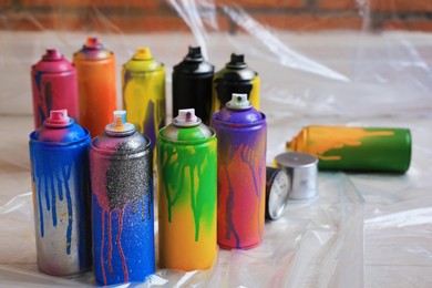 Photo of Used cans of spray paints on floor indoors. Graffiti supplies