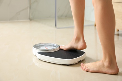 Photo of Woman stepping on floor scales in bathroom, space for text. Overweight problem