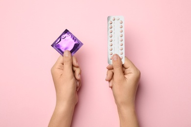 Photo of Woman holding condom and birth control pills on pink background, top view. Safe sex