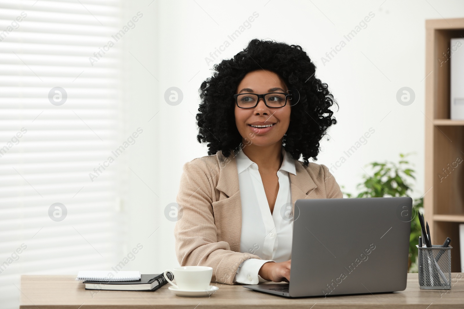 Photo of Happy young woman using laptop at wooden desk indoors. Space for text