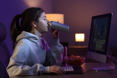 Girl with energy drink playing computer game at home