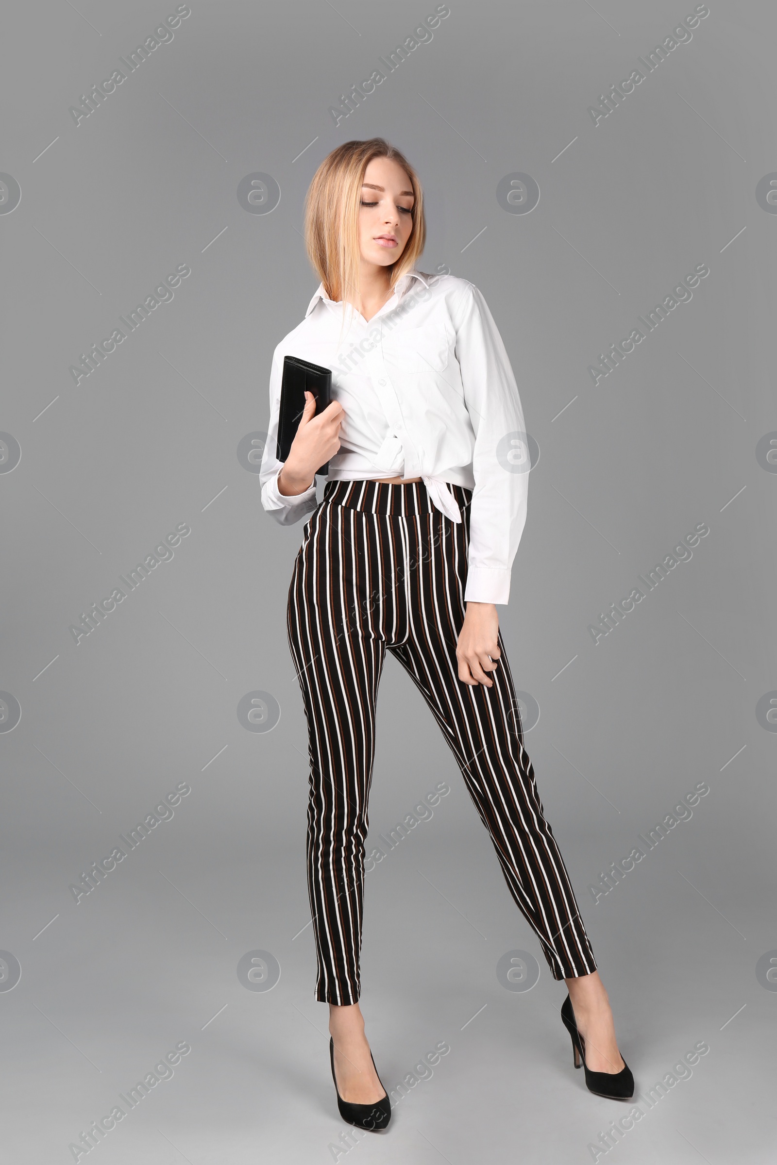 Photo of Young stylish woman in trendy shoes with bag on grey background