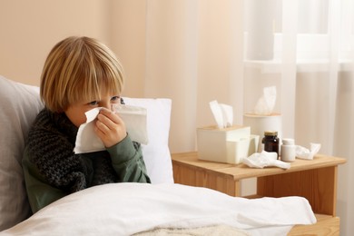 Photo of Boy blowing nose in tissue in bed at home. Cold symptoms