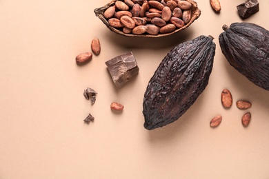 Photo of Cocoa pods with beans and chocolate pieces on beige background, flat lay