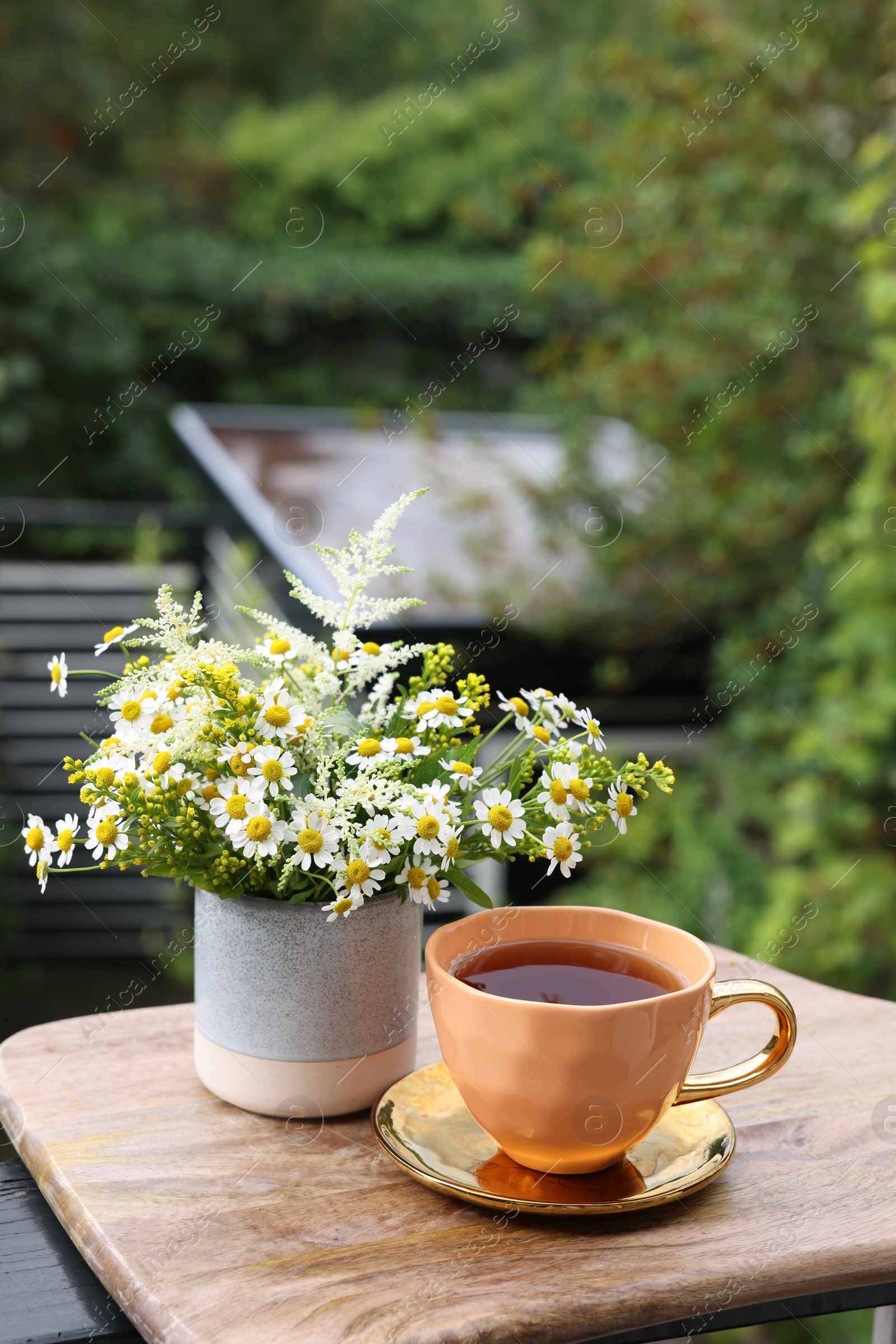 Photo of Cup of delicious chamomile tea and fresh flowers outdoors