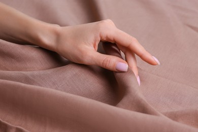 Photo of Woman touching soft light brown fabric, closeup