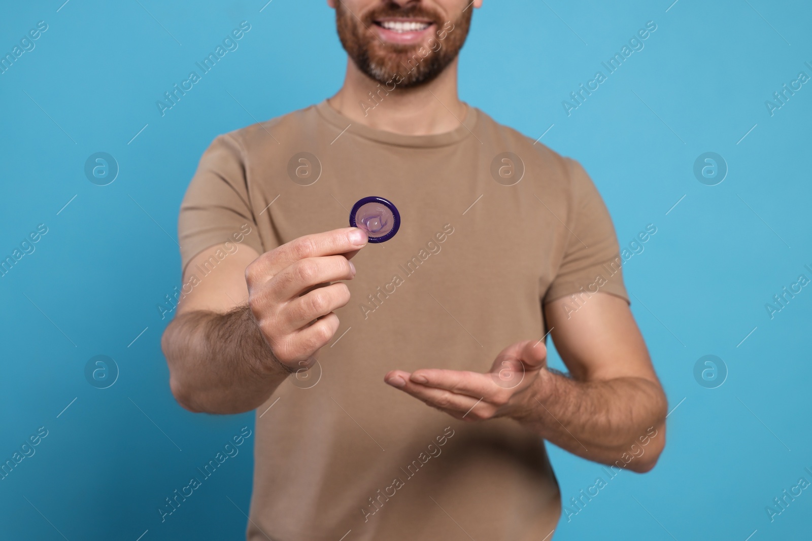 Photo of Man holding condom on light blue background, closeup. Safe sex