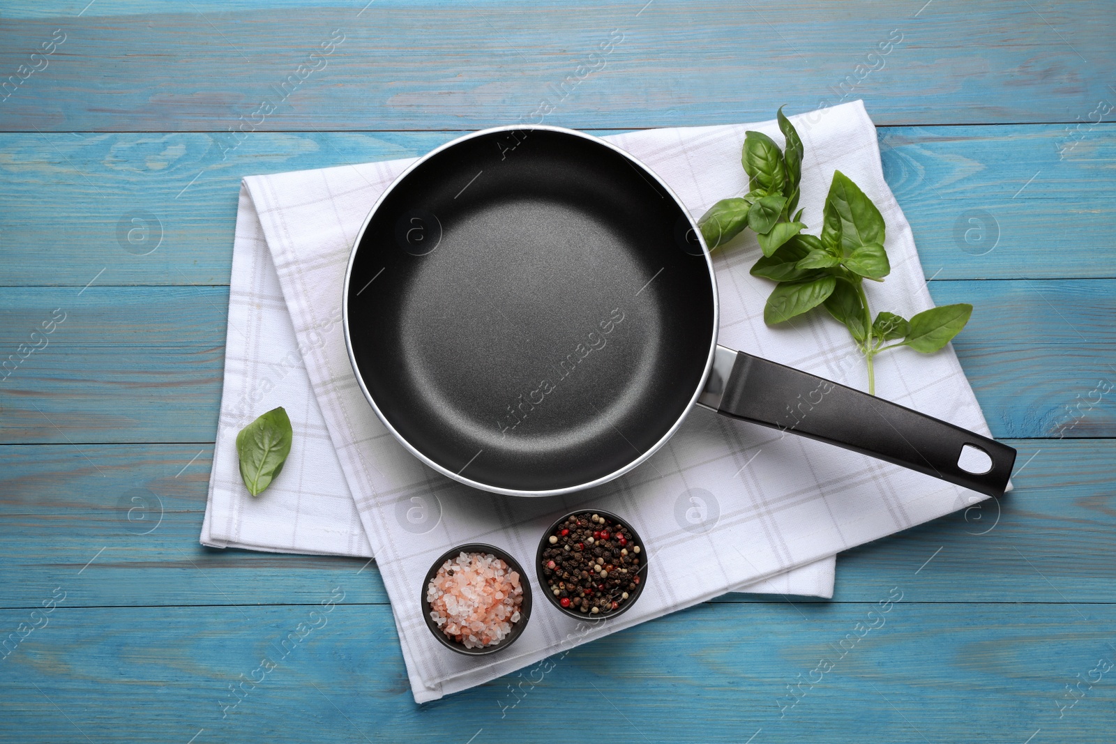 Photo of Frying pan, fresh basil and spices on light blue wooden table, top view