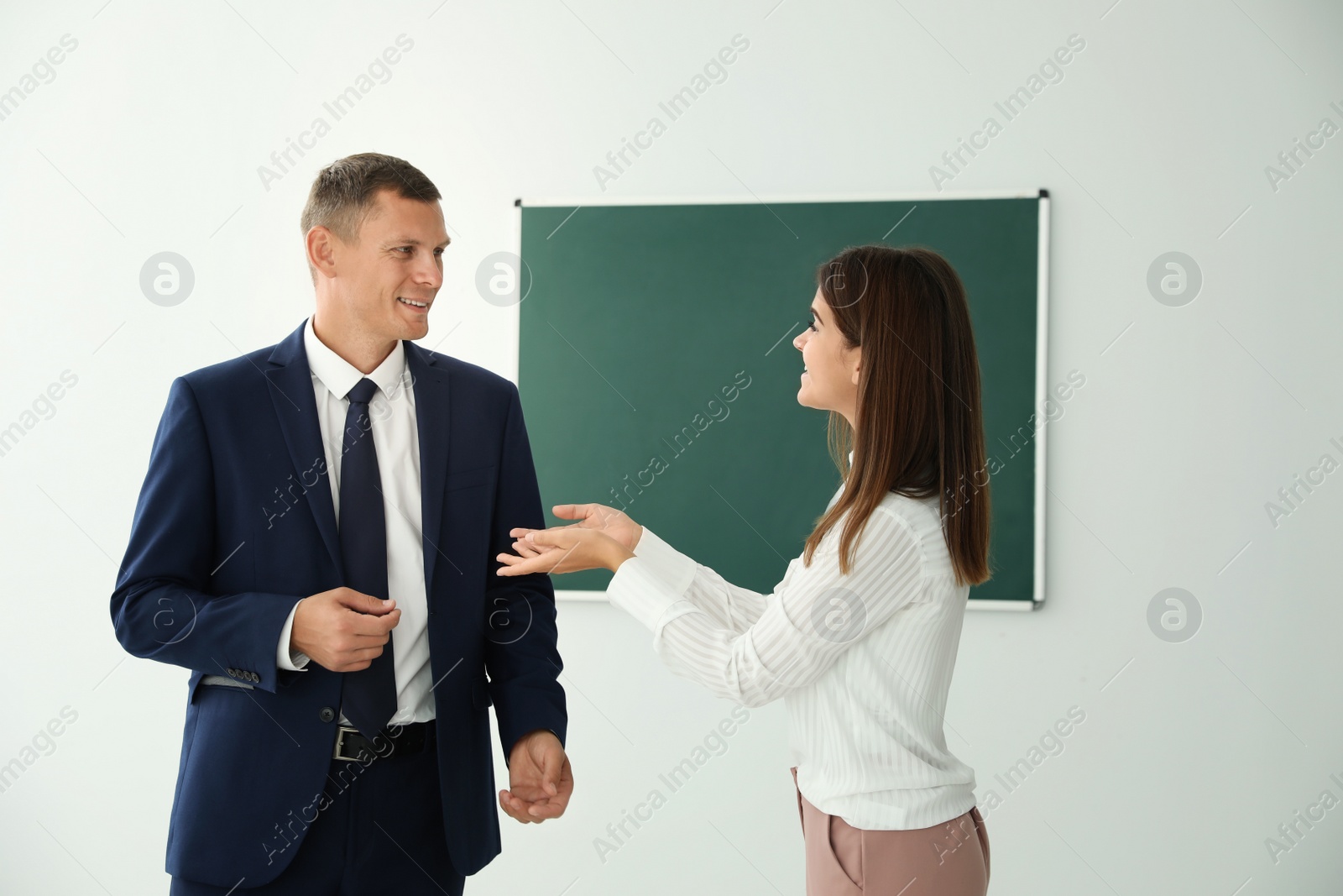 Photo of Man and woman talking near green chalkboard in classroom