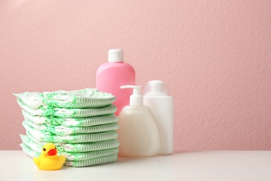 Photo of Stack of diapers, toiletries and toy duck on table against color background, space for text. Baby accessories