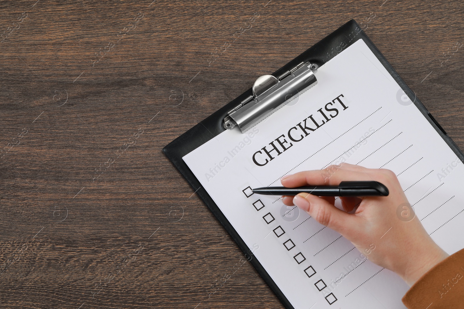 Photo of Woman filling Checklist at wooden table, top view. Space for text